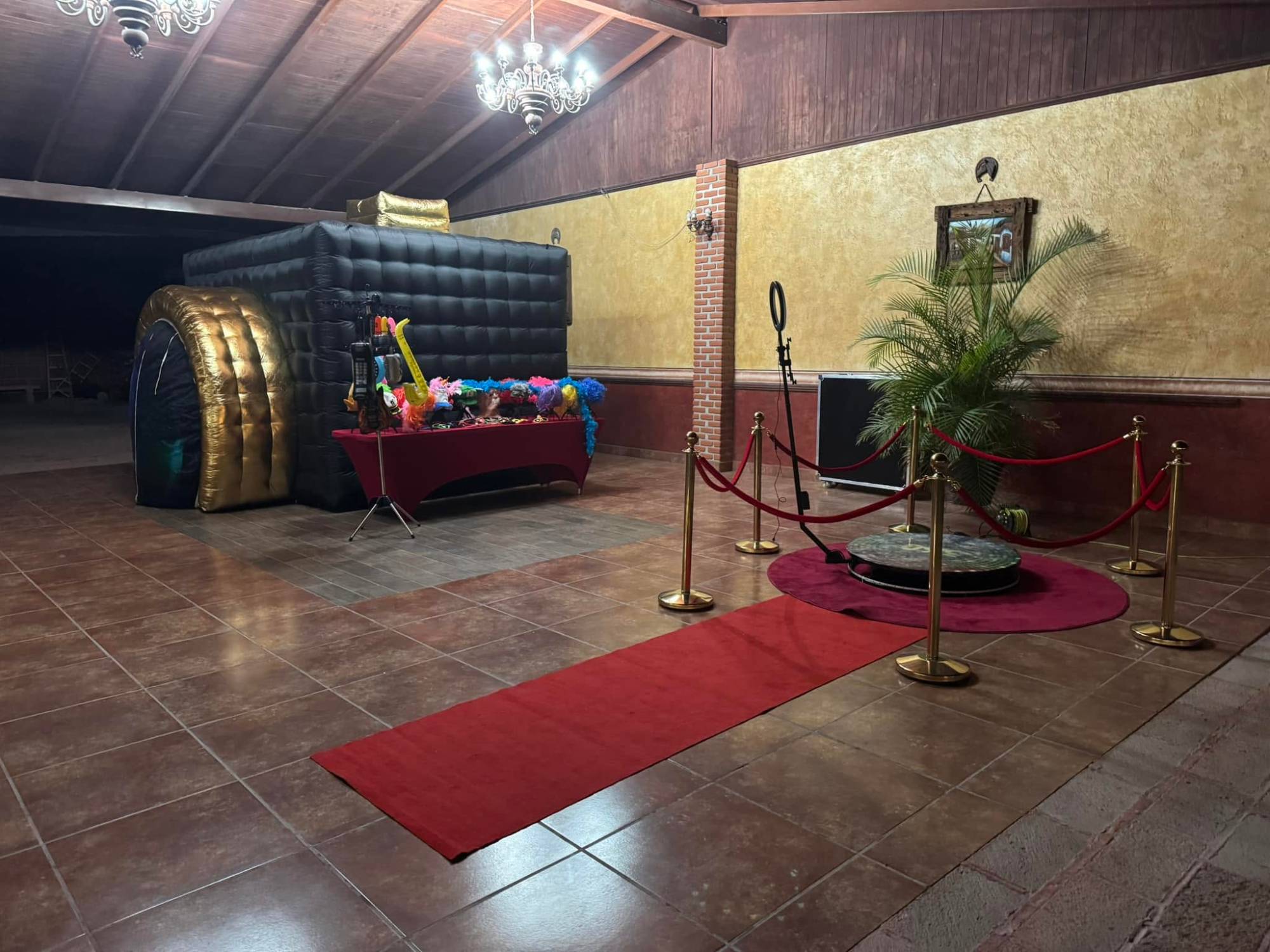 Cabina fotográfica inflable y plataforma 360 con alfombra roja y postes dorados en un evento nocturno