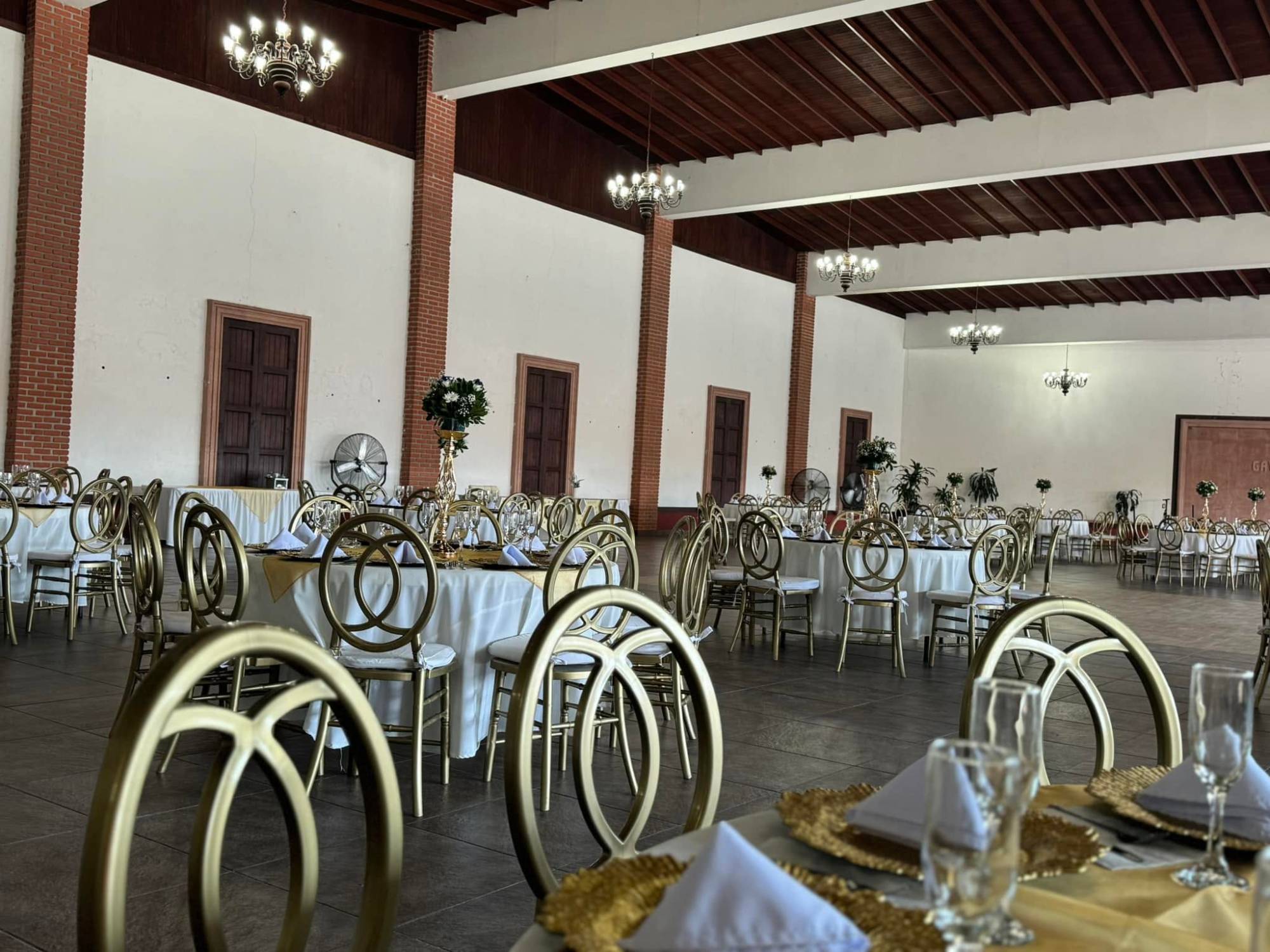 Salón de eventos en Querétaro montado para banquete con sillas doradas, manteles blancos y centros de mesa de flor natural